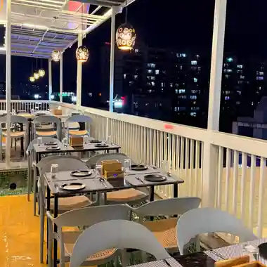 Dining tables along the railing at the Hotel Maruti R South Bopal rooftop restaurant with city lights